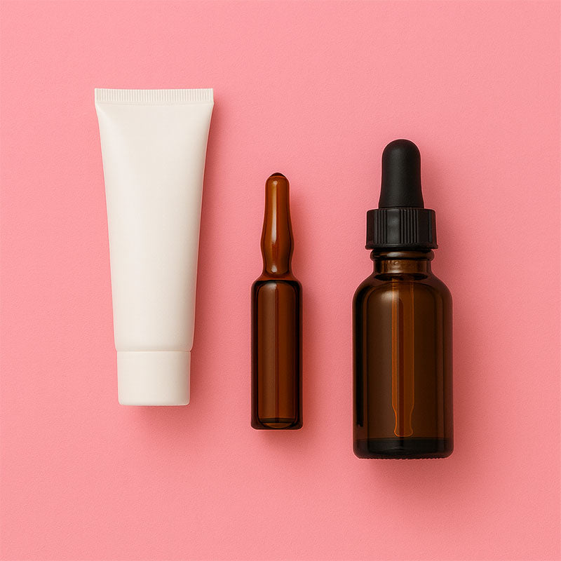 Flacone bianco, fiala ambrata e flacone ambrato con conta giocce nero su sfondo rosa.