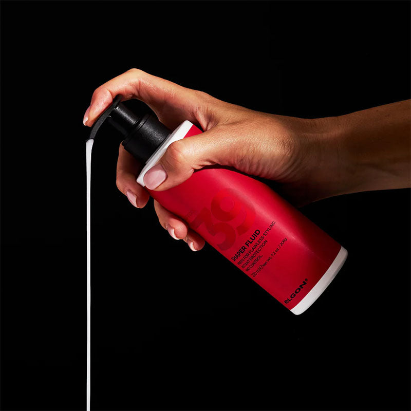 Flacone bianco con etichetta rossa con scritte nere ed erogatore con pompa nero che viene premuto da una mano su sfondo nero.